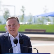 François Legault parle derrière un lutrin en été dehors.