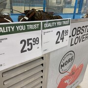 Des affiches de prix dans un supermarché collées sur un aquarium avec des homards.