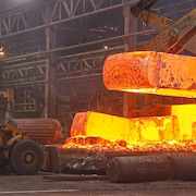 Un bloc d’acier de près de 10 tonnes est transporté par de la machinerie lourde avant d’être forgé sous une presse hydraulique.
