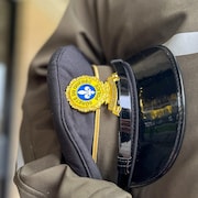 Un policier porte sa casquette sous son bras gauche.