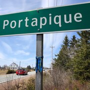 Un tartan bleu et vert est noué autour du poteau qui soutient le panneau annonçant l'entrée de Portapique en bordure d'une route rurale.