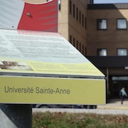 Les mots « Université Sainte-Anne » imprimés sur une plaque posée devant un pavillon de l'université.