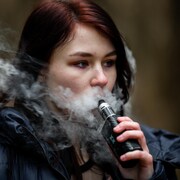 Une jeune femme fume une cigarette électronique.