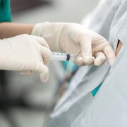 Une anesthésiste fait une injection dans le dos d'une personne avec un cathéter épidural.