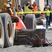 Une marchette à proximité d'une niveleuse. Des rubans jaunes indiquent une scène d'accident.