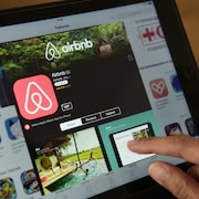 Un doigt s'apprête à appuyer sur le bouton de téléchargement de l'application Airbnb sur une tablette. 
