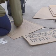 Quelqu'un est à genou au sol et écrit sur une pancarte : Justice for Latjor et Experiencing a mental health crisis should not be a death sentence (Faire face à une crise de santé mentale ne devrait pas être une sentence de mort).