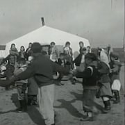 Image en noir et blanc de jeunes Autochtones dansant près d'une tente.  