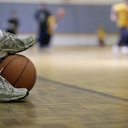 Gros plan sur le pied d'une élève sur un ballon de basketball dans un gymnase. 