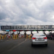Des automobilistes en file avec l'inscription géante « United States of America » au-dessus des guérites du poste frontalier.