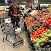 Une femme consulte sa liste d'épicerie dans un rayon de fruits et légumes. 