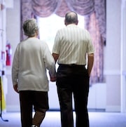 Un couple de personnes âgées marche dans un couloir d'hôpital en se tenant la main.