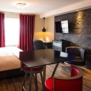 Chambre d'hôtel avec lit, rideau rouge, table, chaises et mur de pierre.
