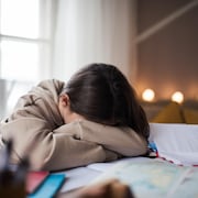 Une jeune fille est allongée sur son bureau dans sa chambre alors qu'elle est censée faire ses devoirs.
