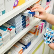 Une pharmacienne tient des boîtes de médicaments dans ses mains derrière un comptoir.