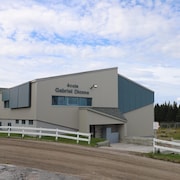 L'école Gabriel-Dionne de Tête-à-la-Baleine, sur la Basse-Côte-Nord, vue de l'extérieur l'été, derrière un drapeau du Québec et devant la cour de récréation et des épinettes.