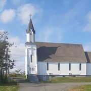 Photo de l'église de Louisbourg prise sur le côté.
Les facades sont en bois blanc, le ciel est gris. En haut du clocher, il y a une croix.