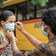 Un père aide sa fille à mettre un masque avant de monter dans un autobus scolaire. 
