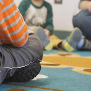 Des enfants assis en cercle par terre sur un tapis, dans une classe.