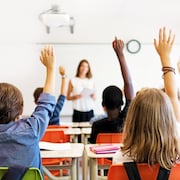 Des étudiants dans une classe lèvent la main pour poser une question au professeur. 