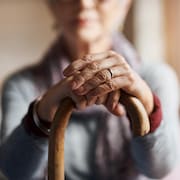 Une personne aînée tient une canne avec ses deux mains.