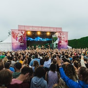Une foule est amassée devant une scène sur laquelle se produisent des artistes.