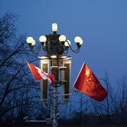 Le soir, un drapeau du Canada et un drapeau de la Chine flottent côte à côte sur un lampadaire allumé.