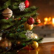 Un sapin de Noël décoré de boules et de guirlandes lumineuses devant un feu de cheminée.