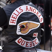 Un homme assis sur sa moto porte une veste qui arbore une tête de mort ailée, symbole des Hells Angels.