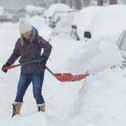 Une femme pellette la neige pour libérer sa voiture dans les rues de Montréal.