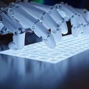 Des mains artificielles tapent sur un clavier d'ordinateur.