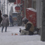 Un homme assis dans la neige sur la rue des Forges en hiver.