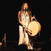 La chanteuse et conteuse innue Kathia Rock, sur scène, chantant et jouant du teweikan.