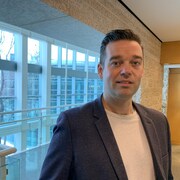 Matthew Gilmour pose devant de larges fenêtres modernes, avec un panorama hivernal.