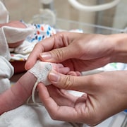 Une infirmière applique un oxymètre sur un nouveau-né. Gros plan avec mise au point sélective sur les mains. (Archives)