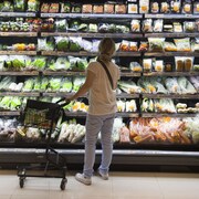 Une personne devant un étal de légumes emballés dans une épicerie.