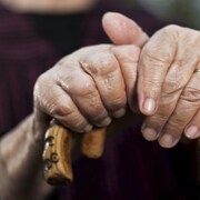 Les mains d'une personne âgée tenant une canne. 