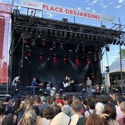 Un groupe de musique sur une scène extérieure; des gens dans la foule le regardent. 