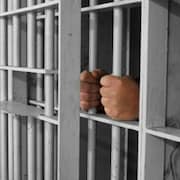 Un homme tient les barreaux d'une cellule de prison.