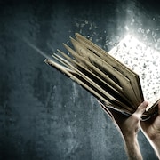 Deux mains tiennent un livre ouvert dont s'échappent des lettres qui volent.