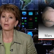 L'animatrice Josée Thibeault présente un reportage sur la dernière «opposition périhélique» survenue entre la Terre et Mars le 28 août 2003.   À l'arrière de l'animatrice se trouve une mortaise de la planète Mars. 