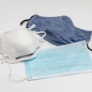 3 types de masques, n95, chirurgical et en tissu, sont posés sur une table blanche.