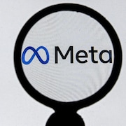Le logo de Meta sur un écran d'ordinateur blanc vu à travers une loupe. 