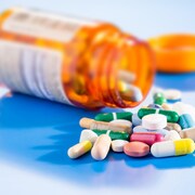 Des pilules de différentes couleurs à côté d'une bouteille de médicaments renversée.
