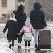 Une famille marche dans la rue en hiver avec une valise.