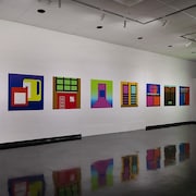 Des tableaux très colorés sur les murs blancs d'une galerie.