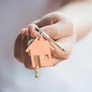 Une main tient des clés avec un porte-clés en forme de maison. 