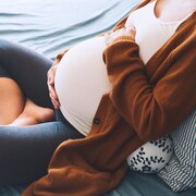 Photo d'une femme enceinte assise en tailleur, les mains sur son ventre.