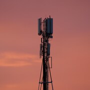 Une tour de télécommunication se découpe en contre-jour sur un ciel de coucher de soleil. 