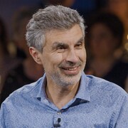 Un homme souriant porte une chemise bleue sur un plateau de tournage. 
